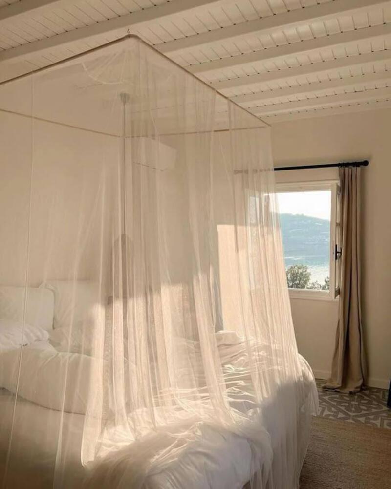 This may contain: a canopy bed with white sheets and pillows in a bedroom next to an open window