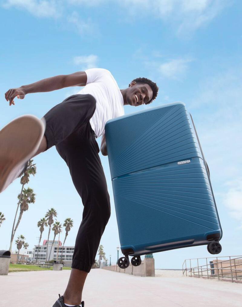 This may contain: a man with a blue suitcase is doing a trick on his skateboard in front of palm trees