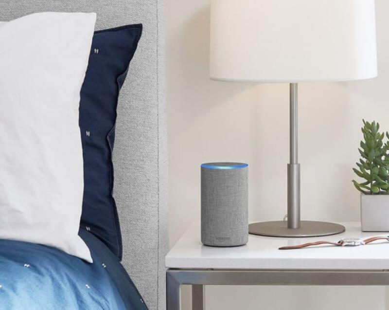 This may contain: an amazon echo sitting on a bedside table next to a plant and a white lamp