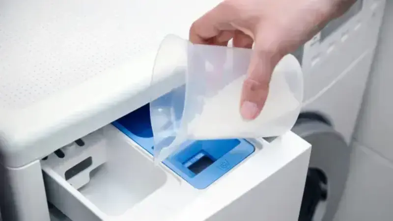 มือกำลังใส่ผงซักฟอกลงในช่องบรรจุของเครื่องซักผ้า