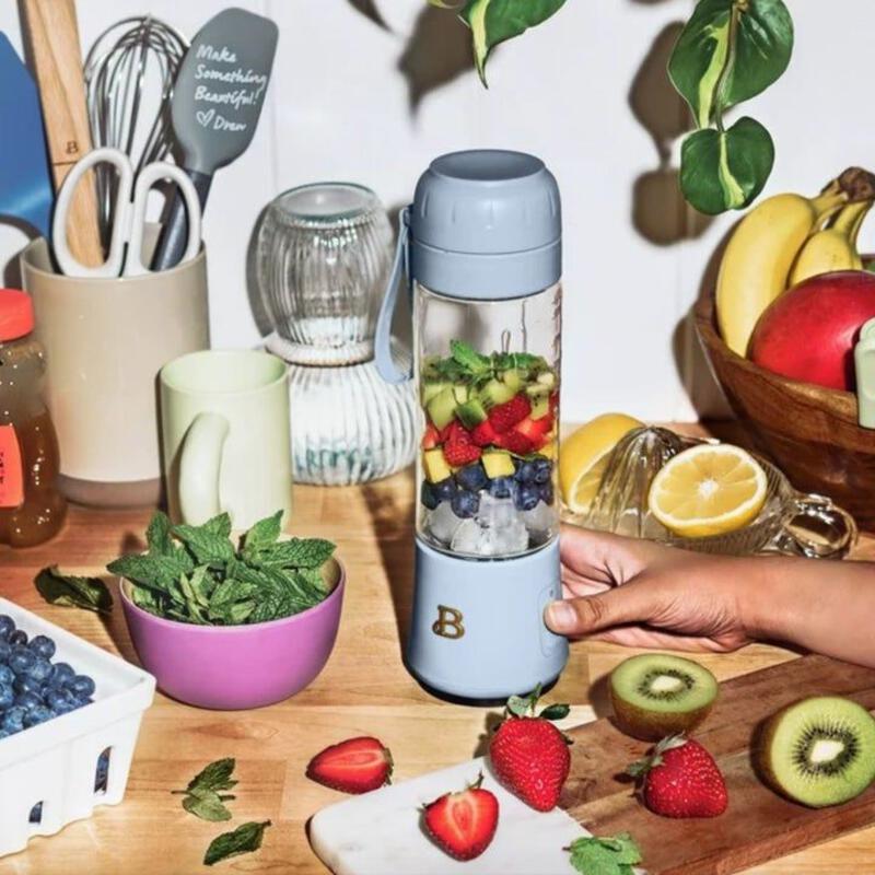 This may contain: a person holding a fruit blender in front of some fruits and vegetables on a table