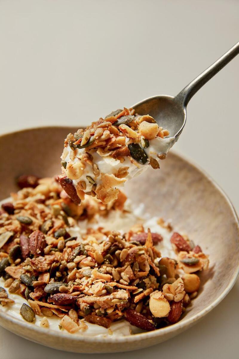 This may contain: a spoonful of granola with nuts and yogurt in a brown bowl