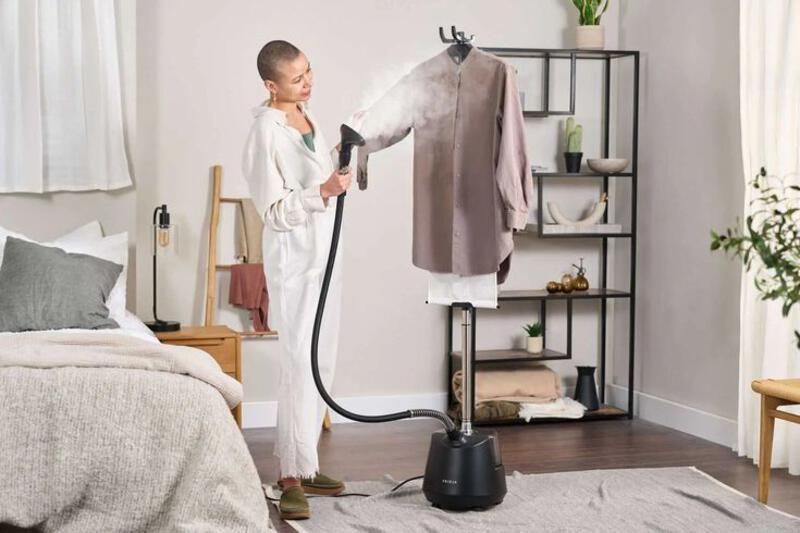 This may contain: a woman is using a steam mop to clean clothes on a rack in her bedroom