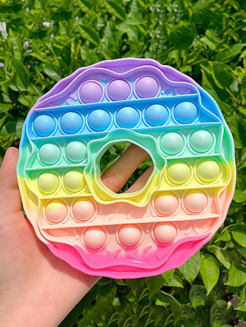 This may contain: a hand holding a multicolored doughnut in front of some green grass and bushes