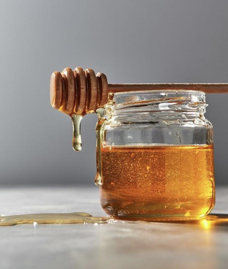 This may contain: honey dripping from a wooden spoon into a jar
