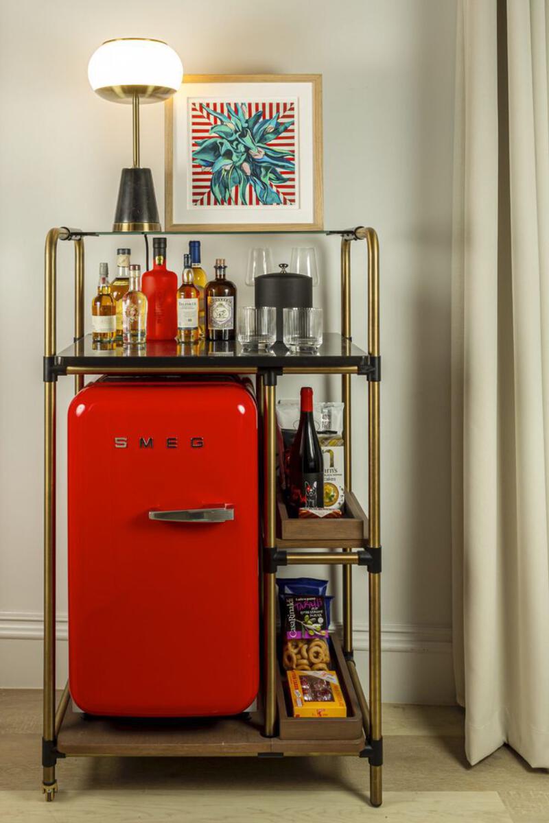 This may contain: a red refrigerator sitting next to a shelf filled with bottles and glasses on top of it