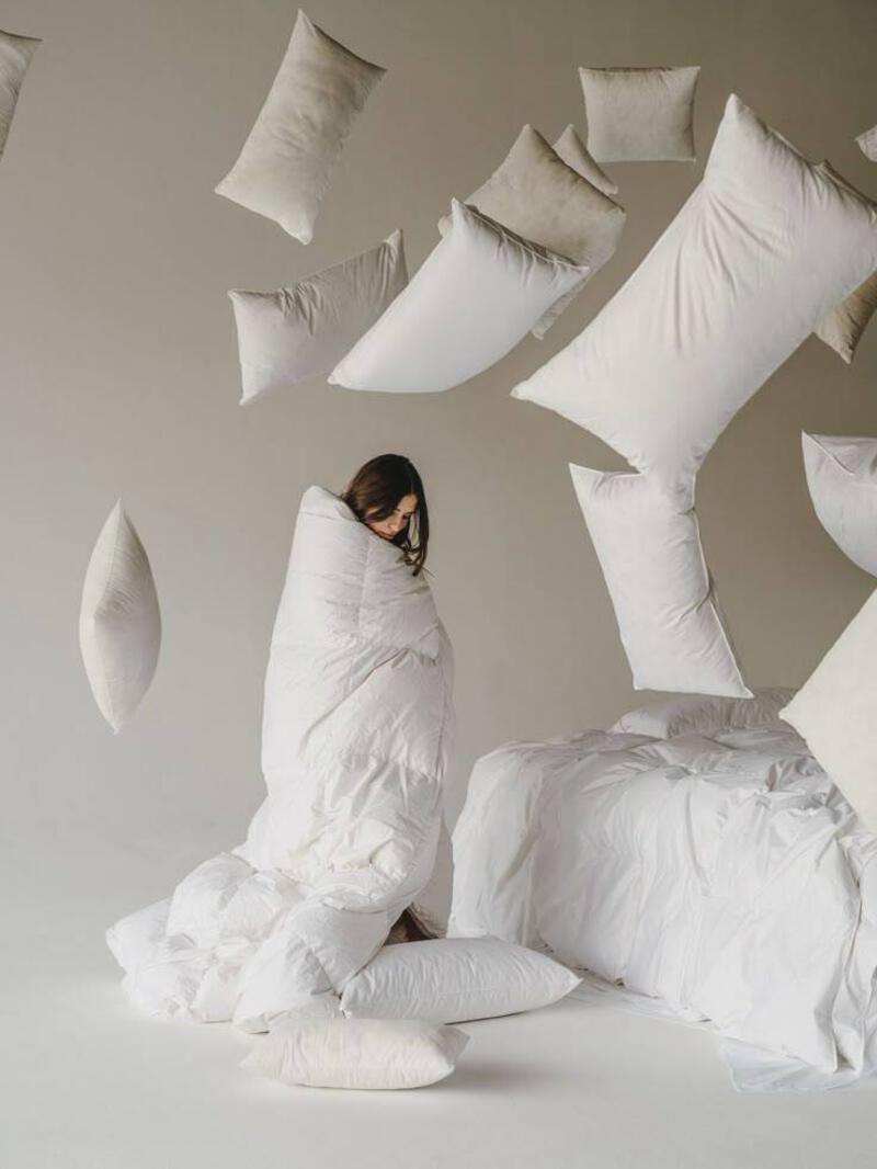 This may contain: a woman sitting on top of a bed surrounded by pillows and pillows flying in the air