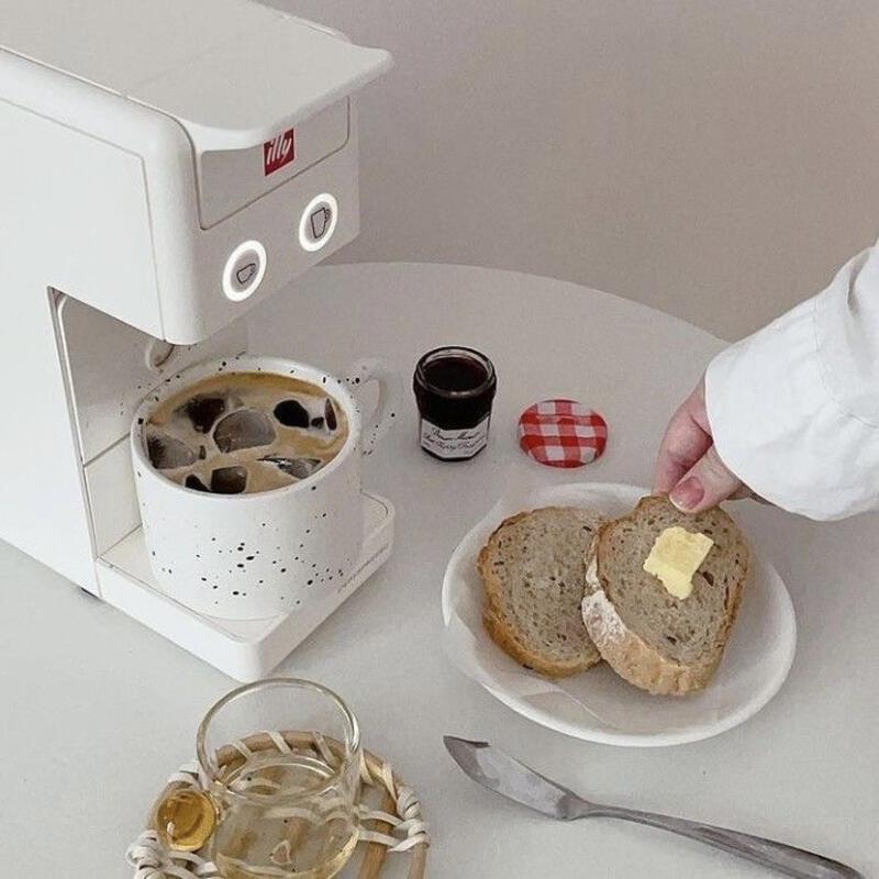 This may contain: a white plate topped with a sandwich next to a cup of coffee and a spoon