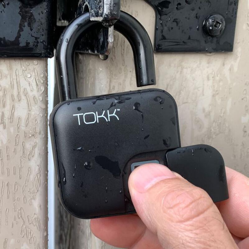 This may contain: a hand holding a black padlock with the word tok written on it, in front of a door