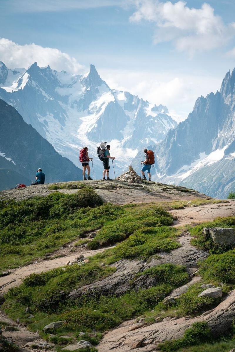 This may contain: three people with backpacks are standing on top of a hill looking at the mountains
