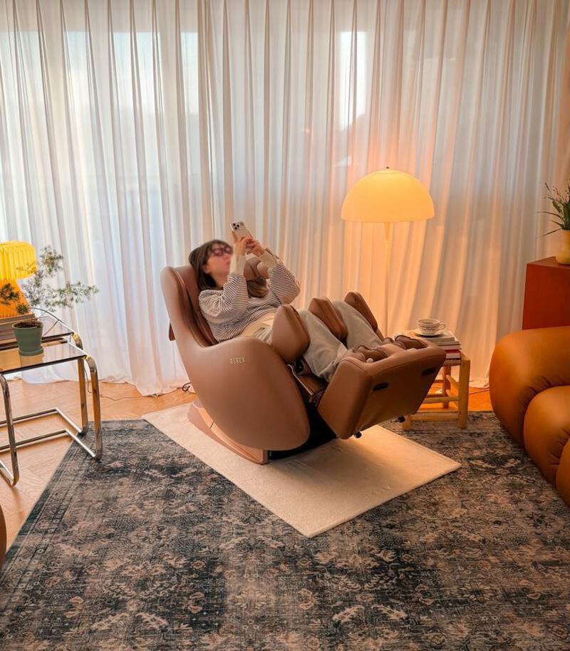 This may contain: a woman sitting in a reclining chair with her feet up on the floor drinking from a bottle