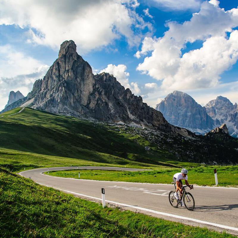 This may contain: a bicyclist rides down the road in front of some majestic mountains and green grass