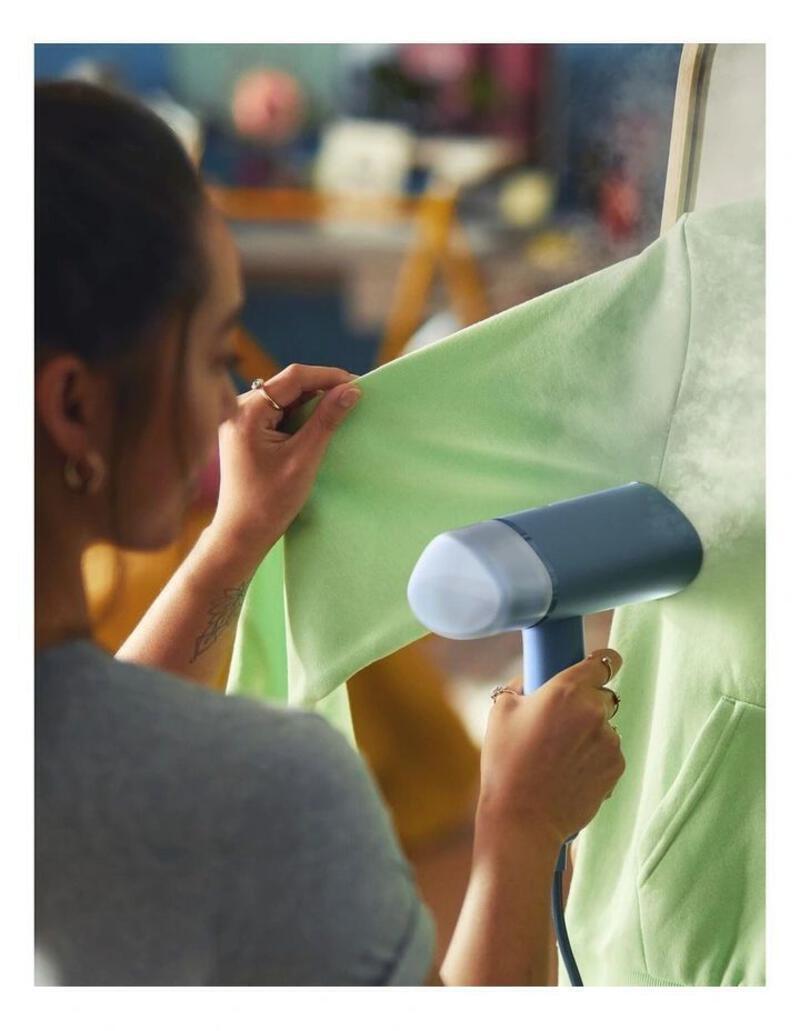 This may contain: a woman working on a green shirt with a hair dryer in front of her