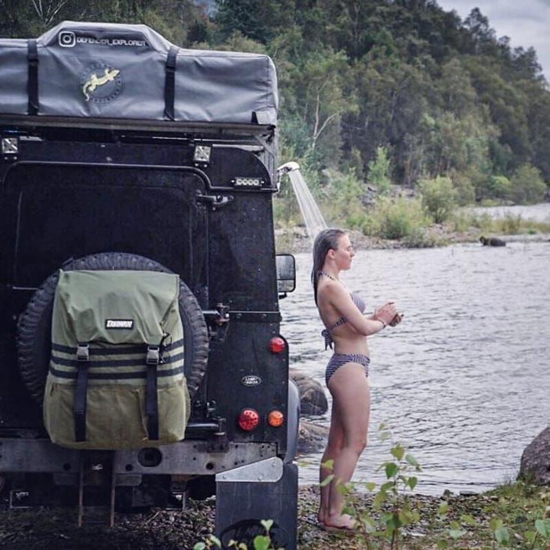 This may contain: a woman standing in front of a truck next to a body of water and trees