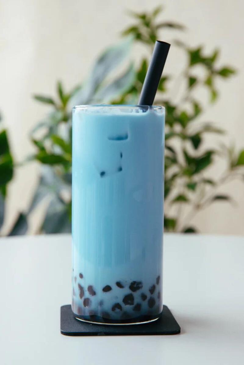 This may contain: a blue drink sitting on top of a white table next to a green leafy plant