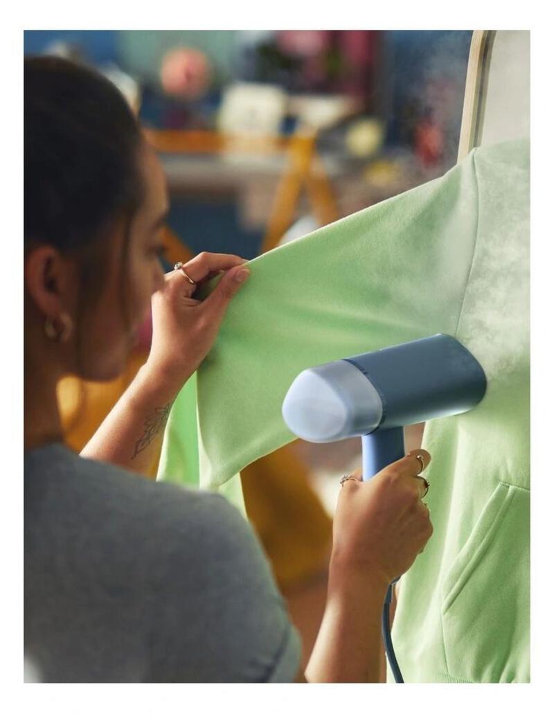 This may contain: a woman working on a green shirt with a hair dryer in front of her