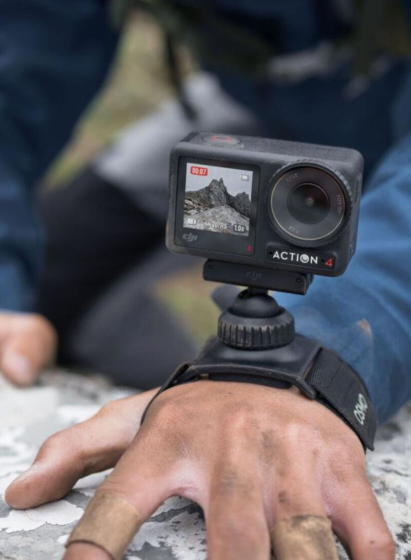 This may contain: a person holding a camera with their hand on the ground and another man sitting in the background